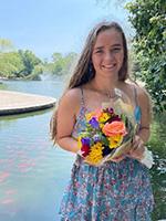 Girl with long dark blonde haor holding flowers in front of river
